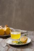 Ginger tea with lemon, ginger root and rosemarry on wooden background. Small glass transparent pitcher with hot drink. Seasonal beverages. Shallow DOF, selective focus, focus on top of pitcher. photo