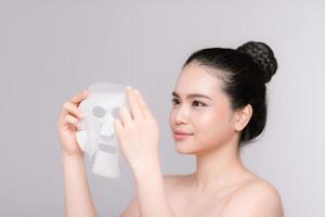 Beauty Skin Care Concept - Beautiful Caucasian Woman applying paper sheet mask on her face white background. photo