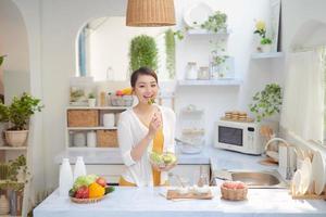 Portrait of smiling young lady cooking fresh organic salad at home in modern kitchen, using and looking at tablet photo