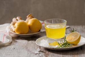 Ginger tea with lemon, ginger root and rosemarry on wooden background. Small glass transparent pitcher with hot drink. Seasonal beverages. Shallow DOF, selective focus, focus on top of pitcher. photo