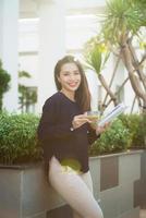 Happy young woman holding book fond of literature analyzing novel during leisure time on terrace of campus cafe in sunny day. photo