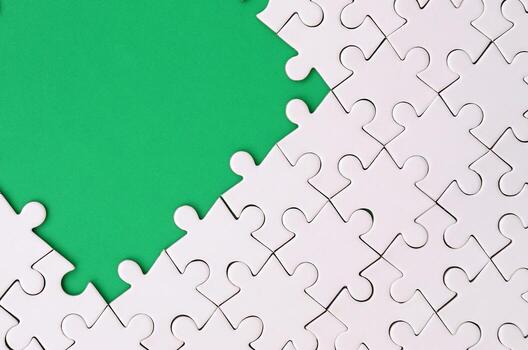 Fragment of a folded white jigsaw puzzle on the background of a green plastic surface. Texture photo with copy space for text