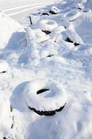 Used and discarded car tires lie on the side of the road, covered with a thick layer of snow photo