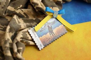 TERNOPIL, UKRAINE - SEPTEMBER 2, 2022 Famous Ukrainian postmark with russian warship and ukrainian soldier as wooden souvenir on army camouflage uniform and national flag photo