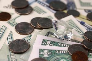 US money bills and coins with large diamond close up. Big amount of dollars and huge transparent gem on table. Business and jewellery photo