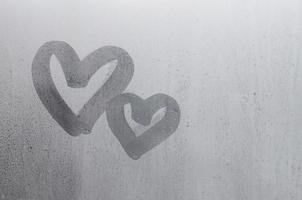 Couple of abstract blurred love heart symbol drawn by hand on the wet window glass with sunlight background. Template for Valentine Day postcards photo