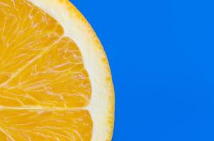 Top view of a one orange fruit slice on bright background in blue color. A saturated citrus texture image photo