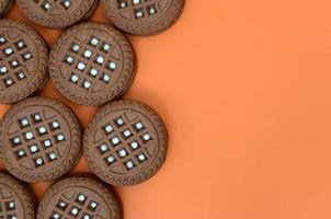 Detailed picture of dark brown round sandwich cookies with coconut filling on an orange surface. Background image of a close-up of several treats for tea photo