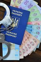 A photograph of a Ukrainian foreign passport, a certain amount of Ukrainian money and police handcuffs. The concept of arresting Ukrainian illegal immigrants while trying to bribe photo