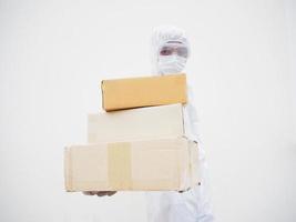 Young man in PPE suite uniform while holding cardboard boxes in medical rubber gloves and mask. coronavirus or COVID-19 concept isolated white background photo