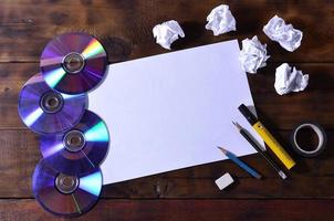 A school or office still life with a white blank sheet of paper and many office supplies. The school supplies lie on a brown wooden background. Place for text photo