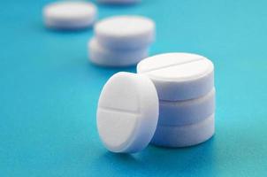 A few white tablets lie on a bright blue background surface. Background image on medical and pharmaceutical topics photo