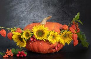 una gran calabaza roja de hokkaido está decorada con girasoles y linternas chinas sobre un fondo oscuro foto