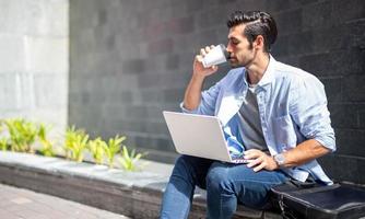 Young caucasian man holding cup of coffee and working on freelance project using portable computer at outer office. photo