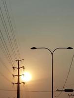 el sol al atardecer con siluetas de postes eléctricos y farolas. foto