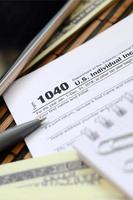 The pen, notebook, smartphone and dollar bills is lies on the tax form 1040 U.S. Individual Income Tax Return. The time to pay taxes photo