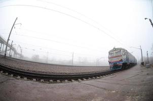 The Ukrainian suburban train rushes along the railway in a misty morning. Fisheye photo with increased distortion