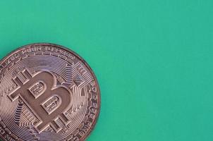 el producto de chocolate en forma de bitcoin físico se encuentra sobre un fondo de plástico verde. modelo de la moneda criptográfica en forma comestible foto