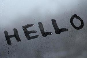 The English word Hello is written with a finger on the surface of the misted glass photo