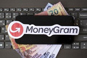 TERNOPIL, UKRAINE - SEPTEMBER 6, 2022 MoneyGram paper logotype lies on black laptop with brazilian reals. Moneygram is American cross border P2P payments and money transfer company photo