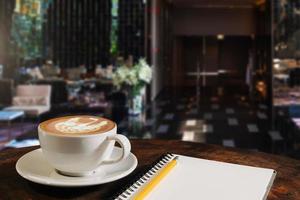 Coffee aroma in cup breakfast morning drink on wooden table in cafe shop with note pad and newspaper background photo