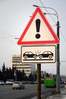 High risk of collision. A road sign with an exclamation point and two cars that crashed into each other photo