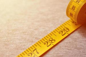 Yellow measuring tape lies on a gray knitted fabric photo