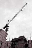 Working tall cranes inside place for with tall buildings under construction against a clear blue sky. Crane and building working progress. Retro tone photo