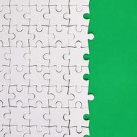 Fragment of a folded white jigsaw puzzle on the background of a green plastic surface. Texture photo with copy space for text