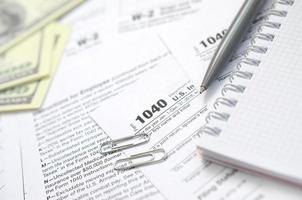 el bolígrafo, el cuaderno y los billetes de dólar se encuentran en el formulario de impuestos 1040 de la declaración de impuestos sobre la renta de las personas físicas. la hora de pagar impuestos foto