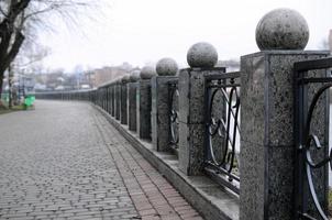 una hermosa cerca de granito con secciones de metal forjado y bolas decorativas como decoración. la valla está construida a lo largo del terraplén de la calle foto