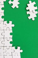 Fragment of a folded white jigsaw puzzle and a pile of uncombed puzzle elements against the background of a green surface. Texture photo with space for text