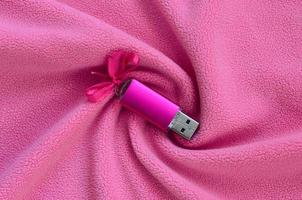 Brilliant pink usb flash memory card with a pink bow lies on a blanket of soft and furry light pink fleece fabric with a lot of relief folds. Memory storage device in women's design photo