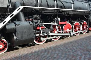 ruedas de la vieja locomotora de vapor negra de la época soviética. el lado de la locomotora con elementos de la tecnología giratoria de trenes antiguos foto