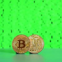 Two gold bitcoins lie on the green surface on the background of the display, which shows the process of mining the crypto currency photo