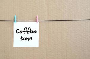 Coffee time. Note is written on a white sticker that hangs with a clothespin on a rope on a background of brown cardboard photo