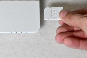 A male hand inserts a white compact SD card into the corresponding input in the side of the white netbook. Man uses modern technologies to store memory and digital data photo