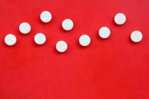 A few white tablets lie on a bright red background surface. Background image on medical and pharmaceutical topics photo
