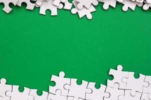 Fragment of a folded white jigsaw puzzle and a pile of uncombed puzzle elements against the background of a green surface. Texture photo with space for text