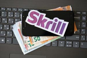 TERNOPIL, UKRAINE - SEPTEMBER 6, 2022 Skrill paper logotype lies on black laptop with euro bills. Payoneer is American financial services company provides online money transfer photo