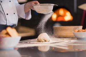 chef sprinkling flour over fresh pizza dough photo