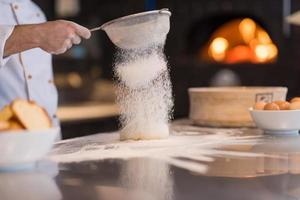 chef sprinkling flour over fresh pizza dough photo