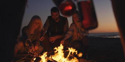 jóvenes amigos haciendo un brindis con cerveza alrededor de una fogata en la playa foto