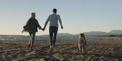 pareja con perro divirtiéndose en la playa el día del otoño