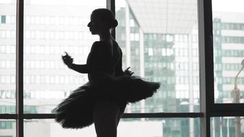 silhouet van een ballerina Aan een achtergrond van de stad een prachtig in beweging dans. in een zwart tutu en pointe schoenen. de beeld van de zwart zwaan van de ballet. langzaam beweging video