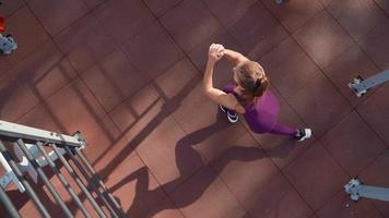 Young athletic woman in a sports purple tracksuit does exercise cross lunges on workout ground in a city park. Fitness outdoors. Slow motion. Top view video