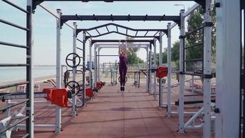 Young athletic woman in a sports purple tracksuit doing abs exercises in a city park. Fitness and workout outdoors. Slow motion video