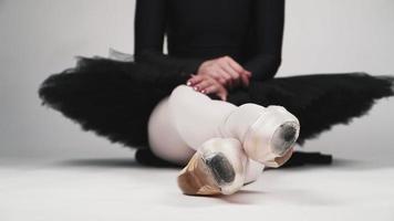 linda jovem dançarina de balé em um tutu preto e sapatilhas, sentado no fundo branco. câmera lenta video