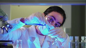 mujer científica en laboratorio haciendo experimentos químicos con líquido azul en tubos de ensayo. extracción de ADN y moléculas. desarrollo de vacunas. investigación, bioquímica, concepto de medicina farmacéutica. video