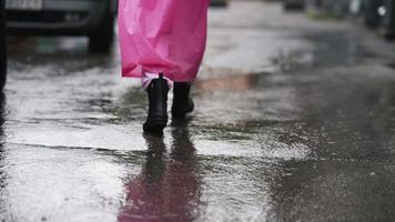 Woman in pink hooded poncho navigates a city street in the rain video